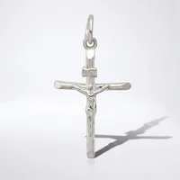 A silver crucifix pendant with a figure of Christ displayed against a white background, casting a shadow to the right.