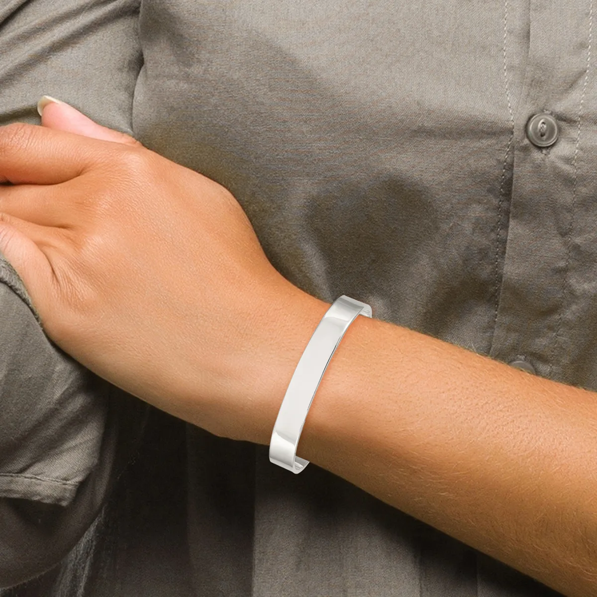 A person wearing a gray button-up shirt displays a white silicone wristband on their wrist.