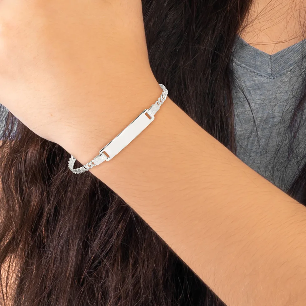 A woman wearing a gray v-neck shirt displays a silver-tone bracelet with a rectangular nameplate and decorative beaded chain links on her wrist.