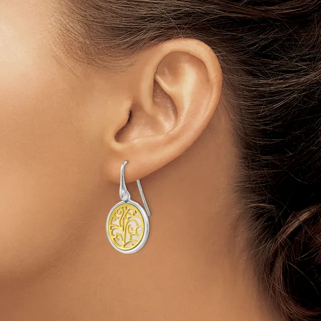 A woman wearing two-tone oval drop earrings with silver outer bands and gold filigree centers hangs from curved silver ear wires.