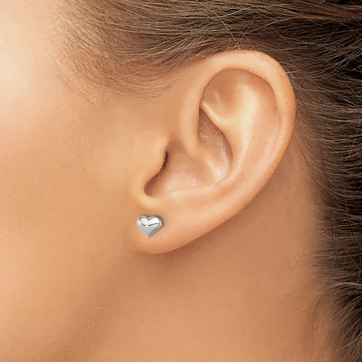 A small silver heart-shaped earring stud in a pierced earlobe, shown in close-up profile view.