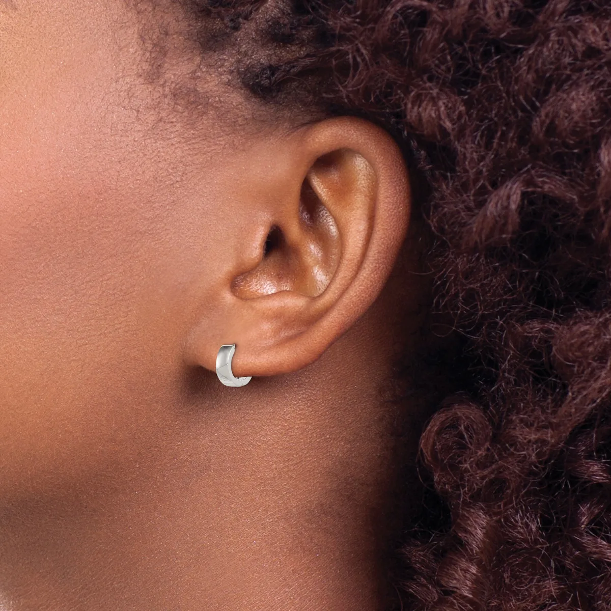A silver crescent-shaped earring worn on the earlobe of a person with dark curly hair and brown skin.