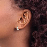 A silver crescent-shaped earring worn on the earlobe of a person with dark curly hair and brown skin.