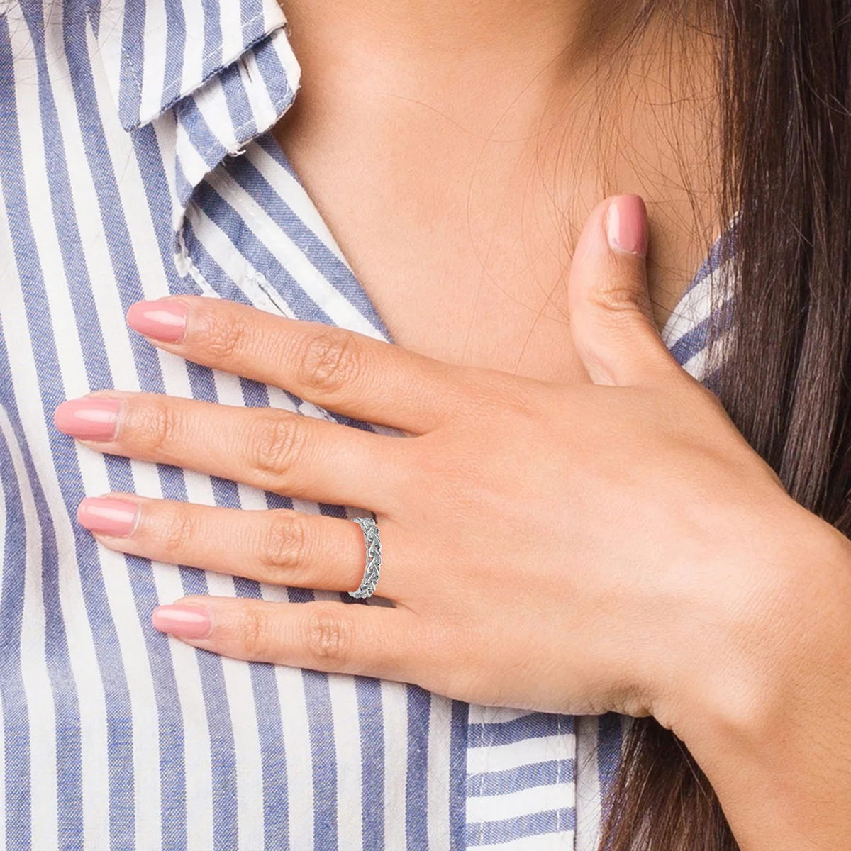 A woman wearing a blue and white striped shirt displays her left hand on her chest, showing a diamond engagement ring and natural nail polish.