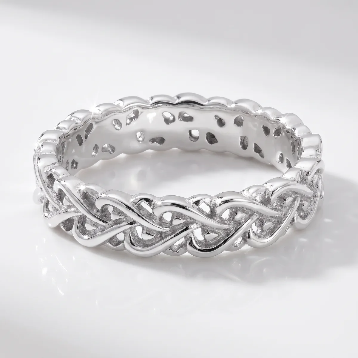 A silver braided twist band ring with an open weave design, photographed on a white reflective surface.