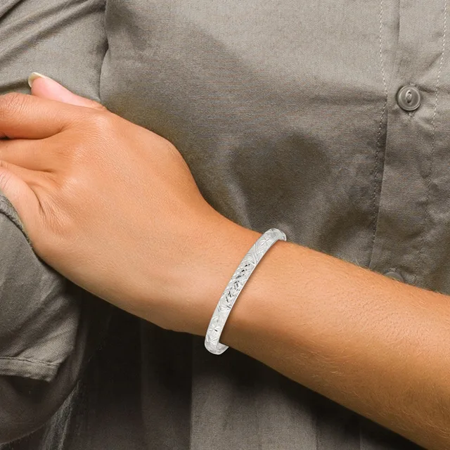 A person wearing a gray button-up shirt displays a white textured bangle bracelet on their wrist.