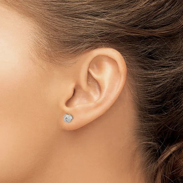 A person wearing a small round stud earring with a textured silver finish in their pierced earlobe.