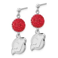 A pair of silver drop earrings with red crystal-encrusted spheres suspended above engraved silver charms shaped like stylized faces.