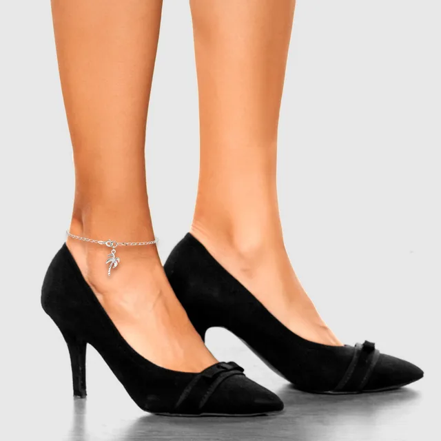 Woman's legs wearing black suede pointed-toe heels with gathered fabric detail at the toe, paired with a silver chain ankle bracelet with a small charm.