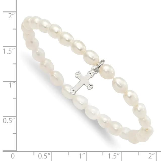 A bracelet made of cream-colored pearl beads with a silver-toned cross charm decorated with small gemstones, displayed against a measurement scale.