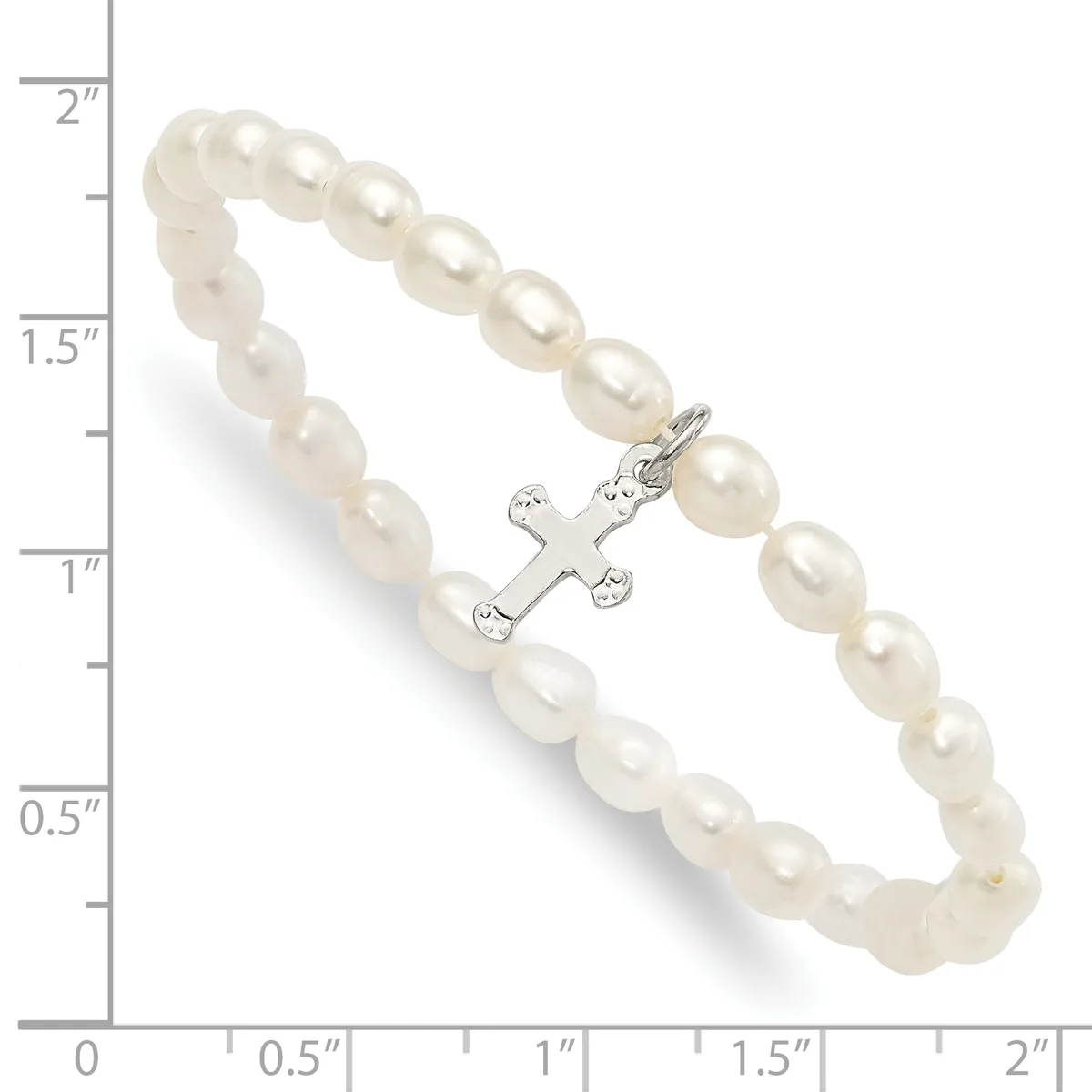 A bracelet made of cream-colored pearl beads with a silver-toned cross charm decorated with small gemstones, displayed against a measurement scale.