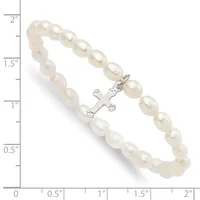 A bracelet made of cream-colored pearl beads with a silver-toned cross charm decorated with small gemstones, displayed against a measurement scale.