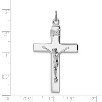 A silver crucifix pendant with a polished cross and detailed corpus figure, shown against a ruler measuring approximately 2 inches in height.
