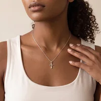 A woman wearing a white sleeveless tank top and a silver chain necklace with a small cross pendant, shown from the shoulders up.