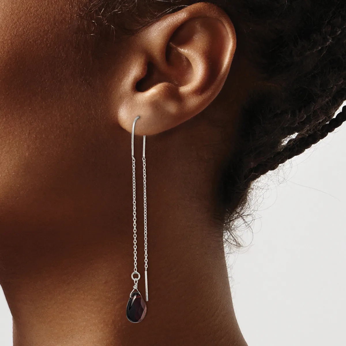 A person wearing long silver chain threaded earrings with small dark stone drops, shown from the side against a neutral background.