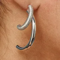 A curved silver earring with a textured top and polished bottom portion hangs from an earlobe against bare skin.