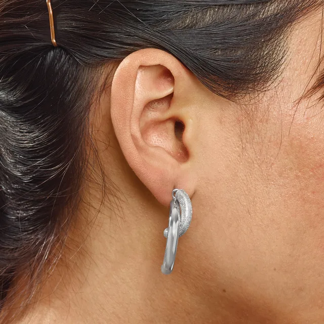 A woman wearing a silver curved hoop earring with a textured finish on her earlobe, with dark hair pulled back.