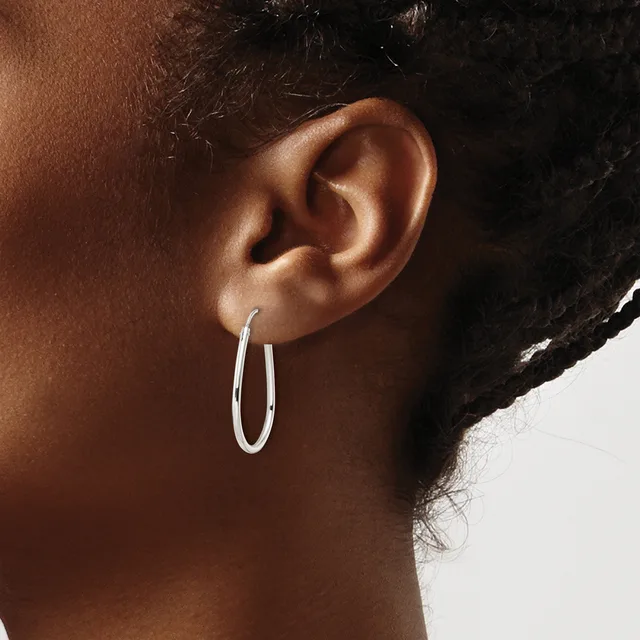 A person wearing a pair of polished silver oval hoop earrings, shown in profile with dark hair pulled back.