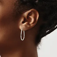 A person wearing a pair of polished silver oval hoop earrings, shown in profile with dark hair pulled back.
