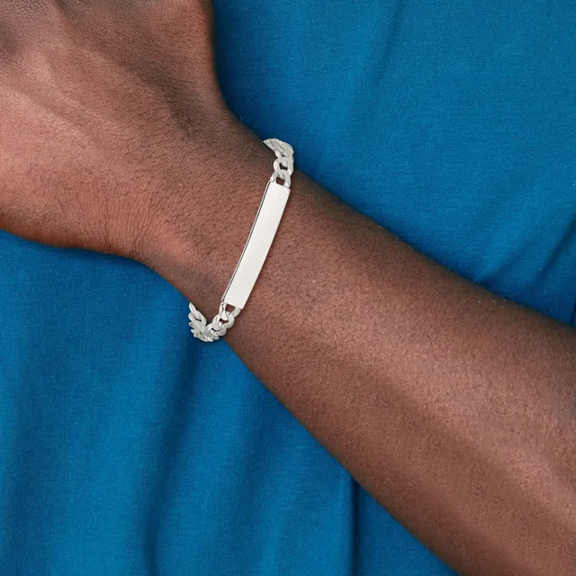 A person wearing a blue shirt displays a silver bracelet with a rectangular plate and decorative linked sections on their wrist.