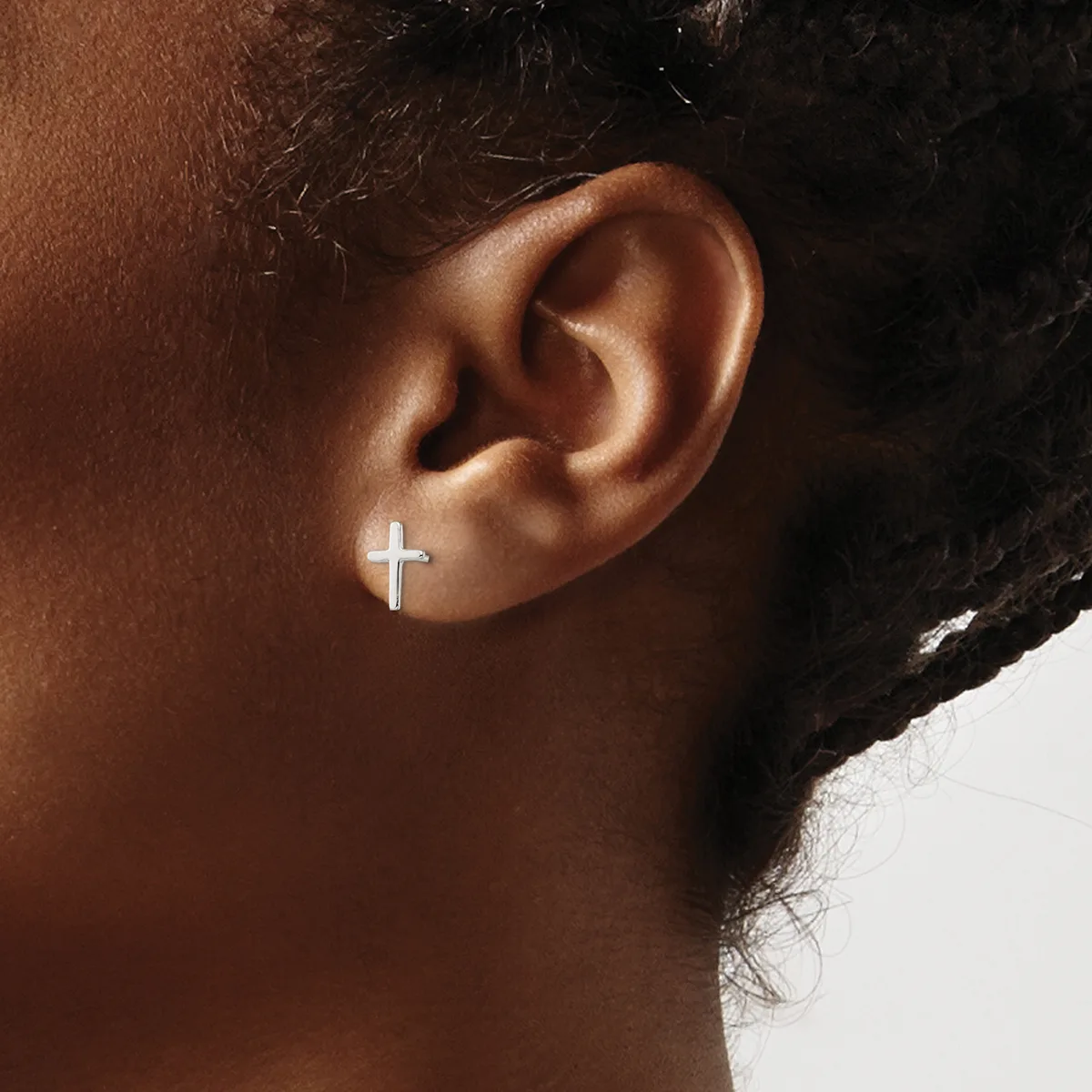 A person wearing a small silver cross earring in their earlobe, shown in profile against a white background.