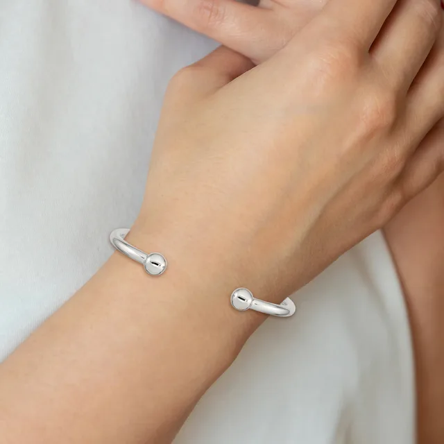 Two silver cuff bracelets with spherical ball details worn on a person's wrist against a white background.
