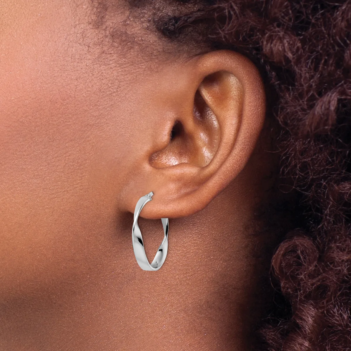 A person wearing a pair of silver twisted hoop earrings in their ear lobes.