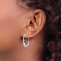 A person wearing a pair of silver twisted hoop earrings in their ear lobes.
