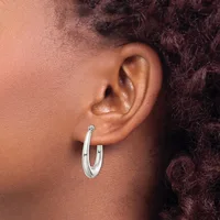 A person wearing a pair of polished silver hoop earrings with a small hallmark on the post, shown from the side profile against their ear.