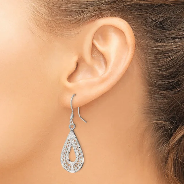 A woman wearing a teardrop-shaped silver dangle earring with a openwork filigree pattern and rhinestone embellishments on a fish hook back.