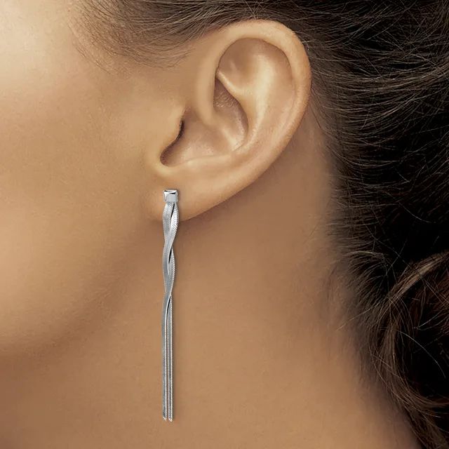 A long, twisted silver rod earring hangs from a woman's pierced earlobe against her bare shoulder and dark hair.