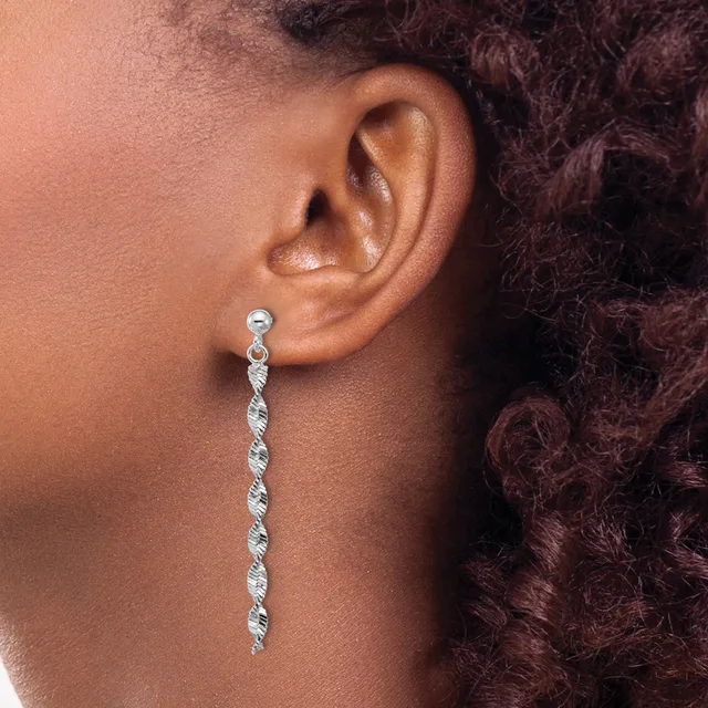 A woman wearing a long silver dangle earring with a twisted spiral design hangs from a stud post in her earlobe.