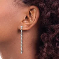 A woman wearing a long silver dangle earring with a twisted spiral design hangs from a stud post in her earlobe.