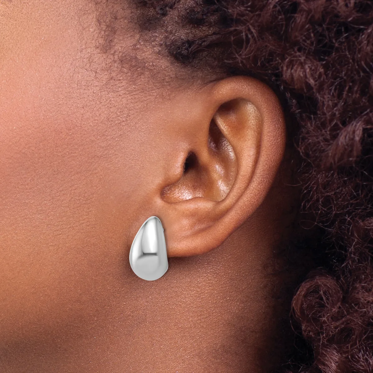 A person wearing a polished silver teardrop-shaped earring on their earlobe, shown in profile against their neck and shoulder.