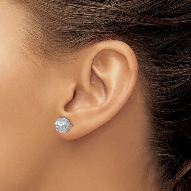 A person wearing a small round silver stud earring with a textured finish in their earlobe.