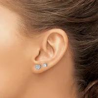 A person wearing two diamond stud earrings in their pierced earlobes, one heart-shaped and one round, shown from the side profile.