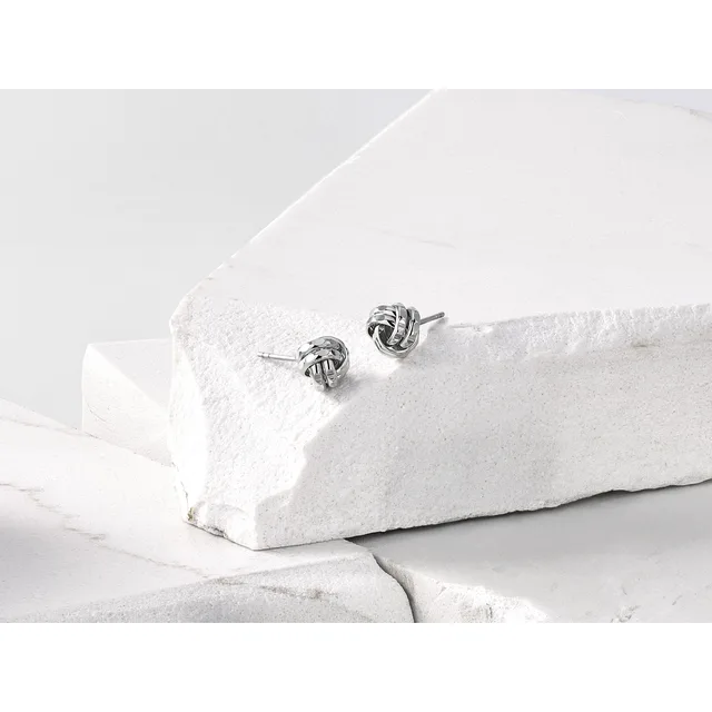 Pair of silver knot stud earrings displayed on white textured stone blocks.
