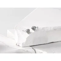 Pair of silver knot stud earrings displayed on white textured stone blocks.