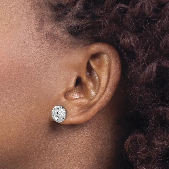 A person wearing a single round diamond stud earring in their pierced earlobe, shown in profile view against their shoulder and dark curly hair.