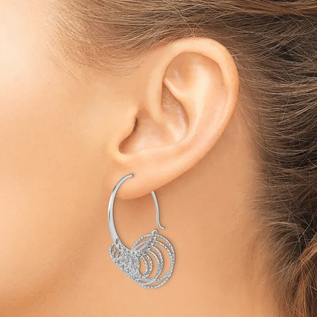 Silver hoop earrings with spiral and diamond-patterned circular charms hanging from the ear lobes.
