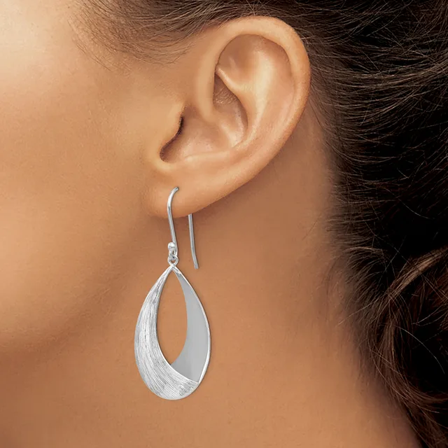 A woman wears a pair of silver teardrop earrings with a brushed texture and threader-style hooks through her ears.