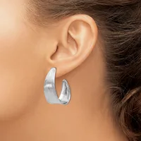 Silver curved hoop earrings with a brushed finish worn on a person's ear.