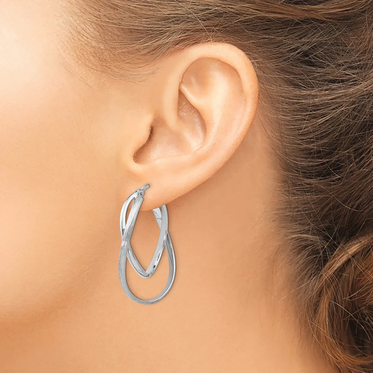 A woman wearing silver twisted hoop earrings, shown from the side view of her ear and neck.