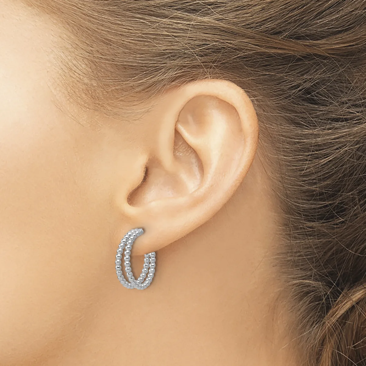 A woman wearing diamond hoop earrings with a textured surface, shown from the side view of her ear and upper shoulder.