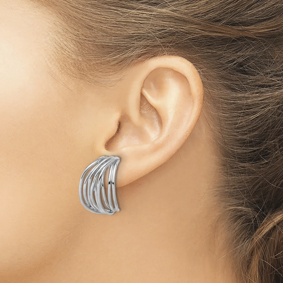 A silver curved cuff earring with parallel grooved lines worn on a person's ear.