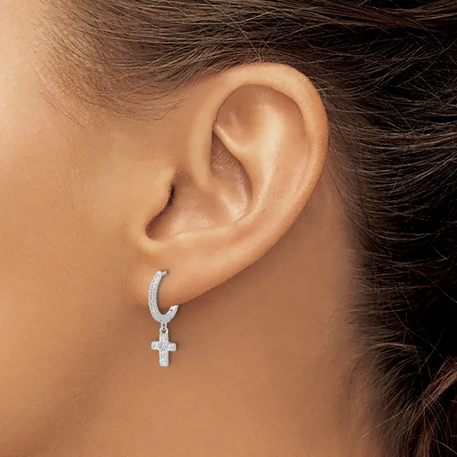 A person wearing a silver hoop earring with a small cross pendant hanging from it in their pierced earlobe.