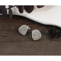 Two silver mesh dome-shaped earrings displayed on a dark wooden surface next to a white bowl and dark green eucalyptus leaves.