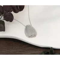 Silver teardrop pendant with textured mesh pattern on a delicate chain, displayed on white ceramic dish with dark foliage beside it.