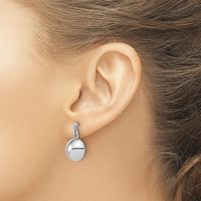A woman wearing a silver drop earring with a polished spherical pendant and decorative connector, shown from the side view of her ear and neck.