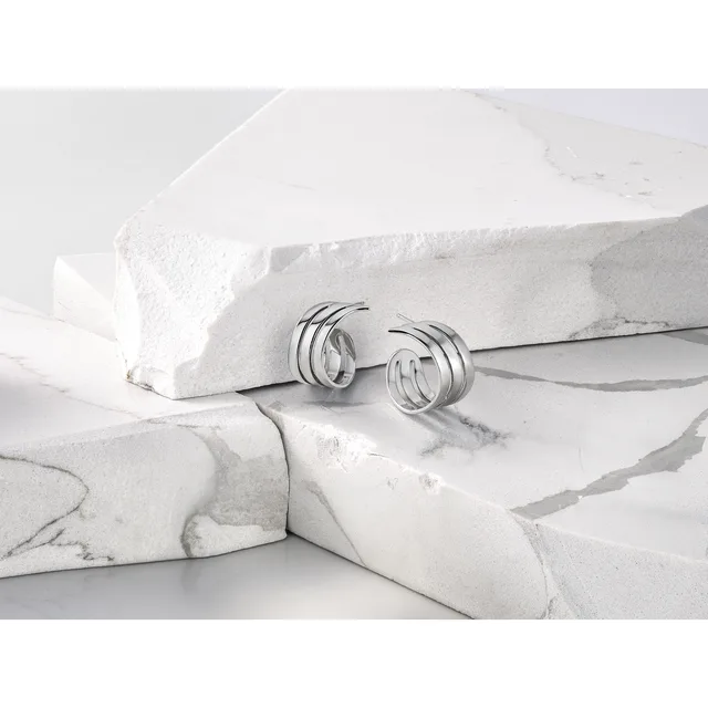 Silver hoop earrings with triple-band design displayed on white marble surfaces and draped fabric.
